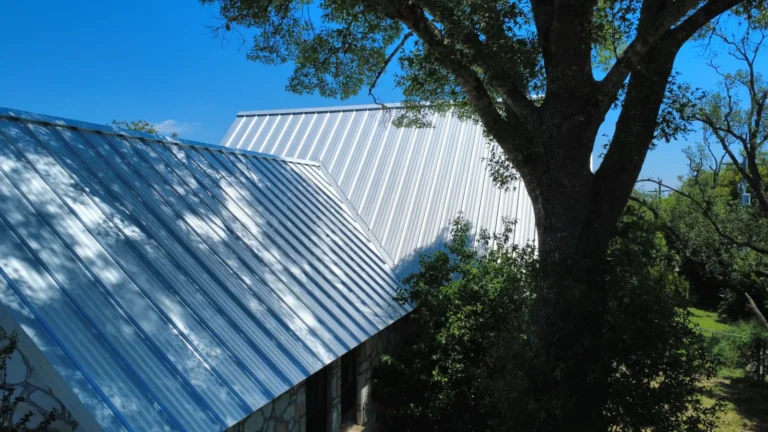 Close-up of Galvalume standing seam panels under a large shade tree on a limestone home in Dripping Springs, TX