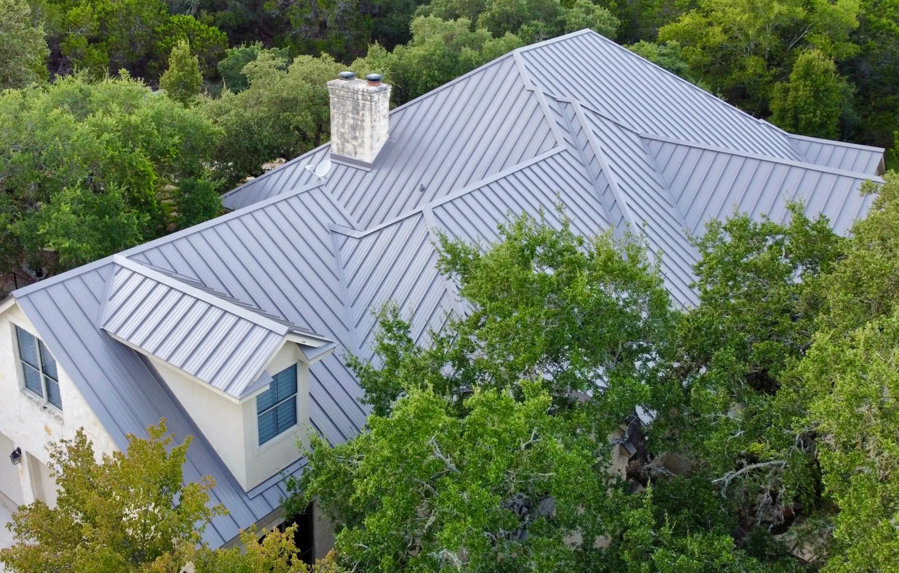 Standing seam metal roof on a limestone home surrounded by oak trees in Austin, TX