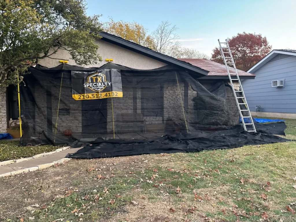 Catch-All netting set up across the front of a single-story stone home before a roof tear-off, covering the windows, entry, and lawn