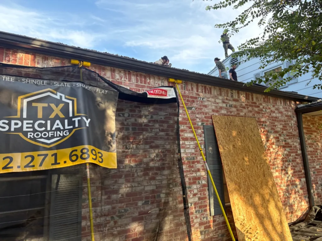 Roofing crew working on a brick home while Catch-All netting with the Texas Specialty Roofing banner protects the wall below