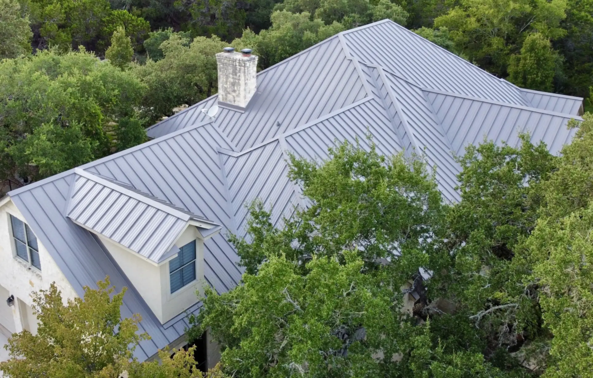 Standing seam metal roof on a limestone home surrounded by oak trees in Dripping Springs, TX