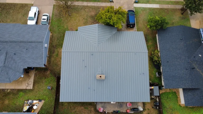 Top-down drone view of a new gray standing seam metal roof with a chimney cricket on a single-story home between two shingle roofs