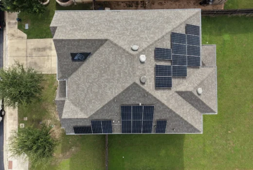 Top-down aerial view of a large asphalt shingle roof with several rooftop solar panel arrays and roof vents.
