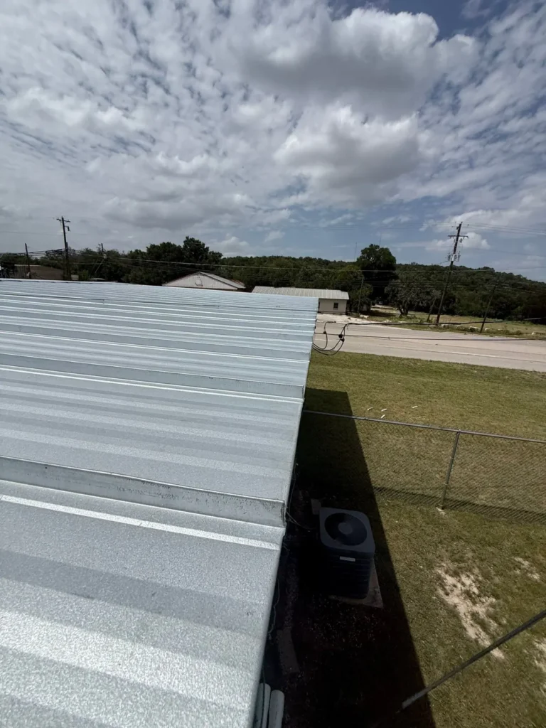 New silver metal roof on a commercial building in Burnet, TX, seen from the eave above the AC unit