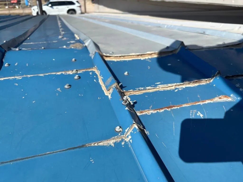 Old metal roof section in Burnet, TX with separated seams, cracked sealant, and rust along the panel laps