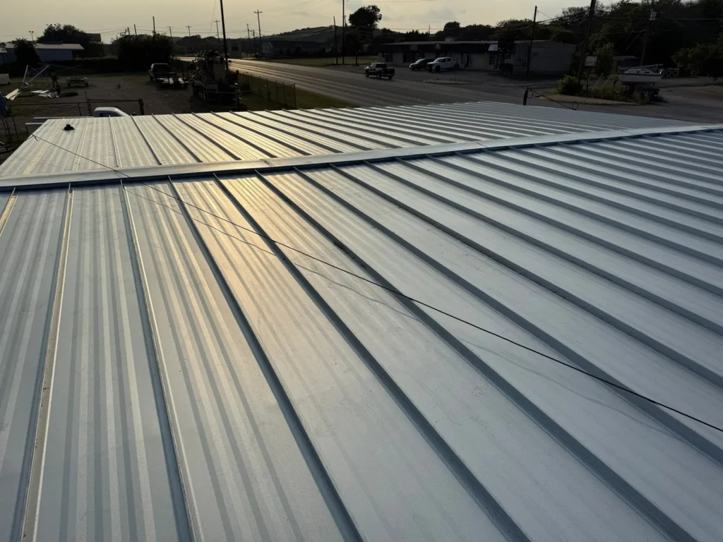 Finished standing seam metal roof with ridge cap on a commercial building in Burnet, TX at sunset