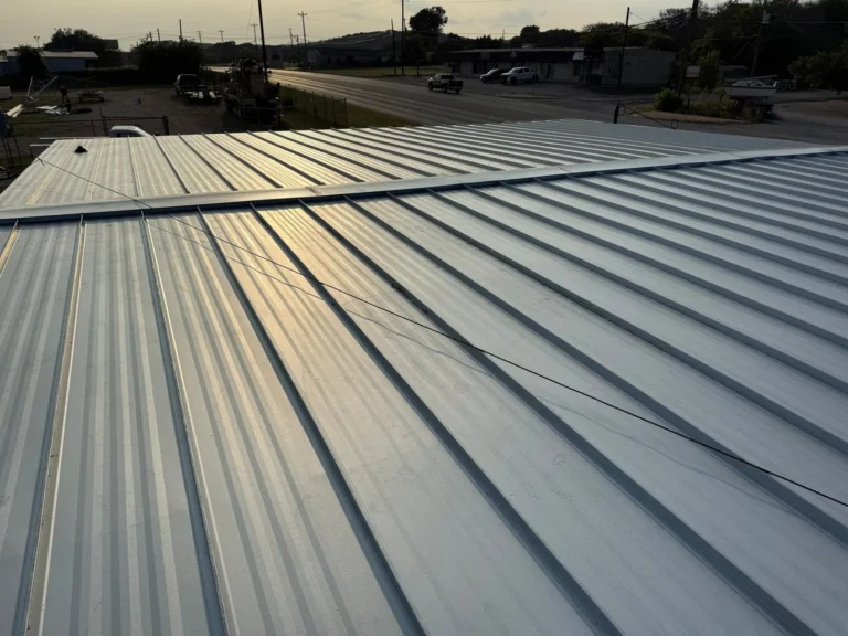 Finished standing seam metal roof with ridge cap on a commercial building in Burnet, TX at sunset