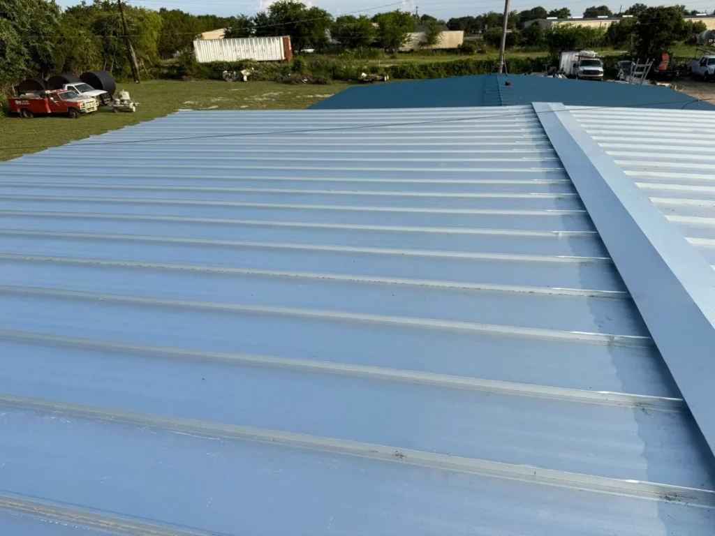 New silver metal roof panels meeting at a ridge cap on a commercial building in Burnet, TX