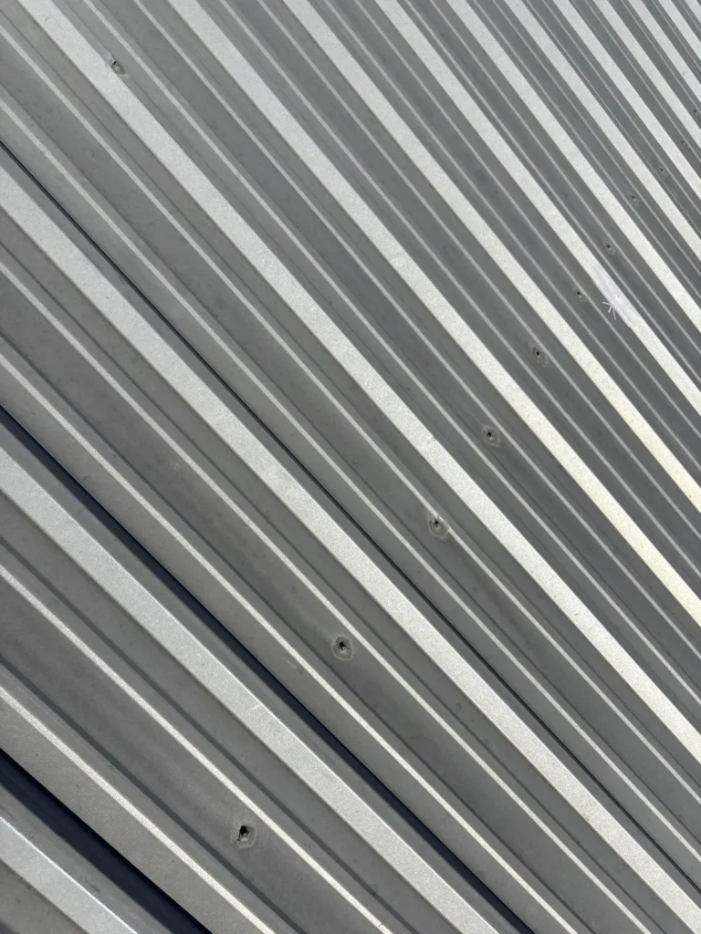 Close-up of older metal roof panels with exposed fastener holes on a commercial building in Burnet, TX
