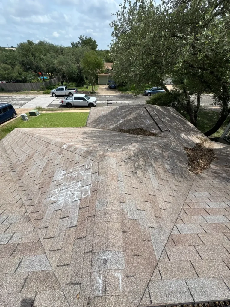 Aging shingle roof in Cedar Park, TX with inspection notes in chalk and leaf debris collecting in the valleys under an oak tree