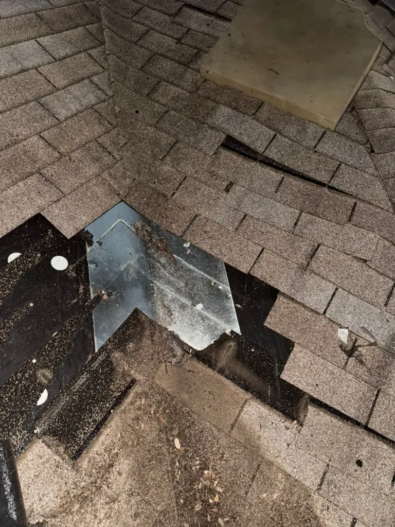 Old shingles being removed around worn metal valley flashing at first light during a roof replacement in Cedar Park, TX