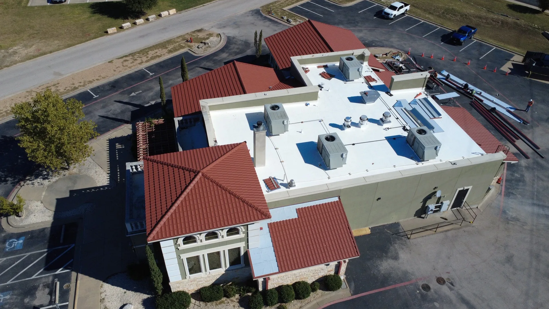 Aerial view of a completed commercial metal roofing project with red Worthouse metal tile on the sloped roofs and a white Versico PVC flat roof with rooftop HVAC units