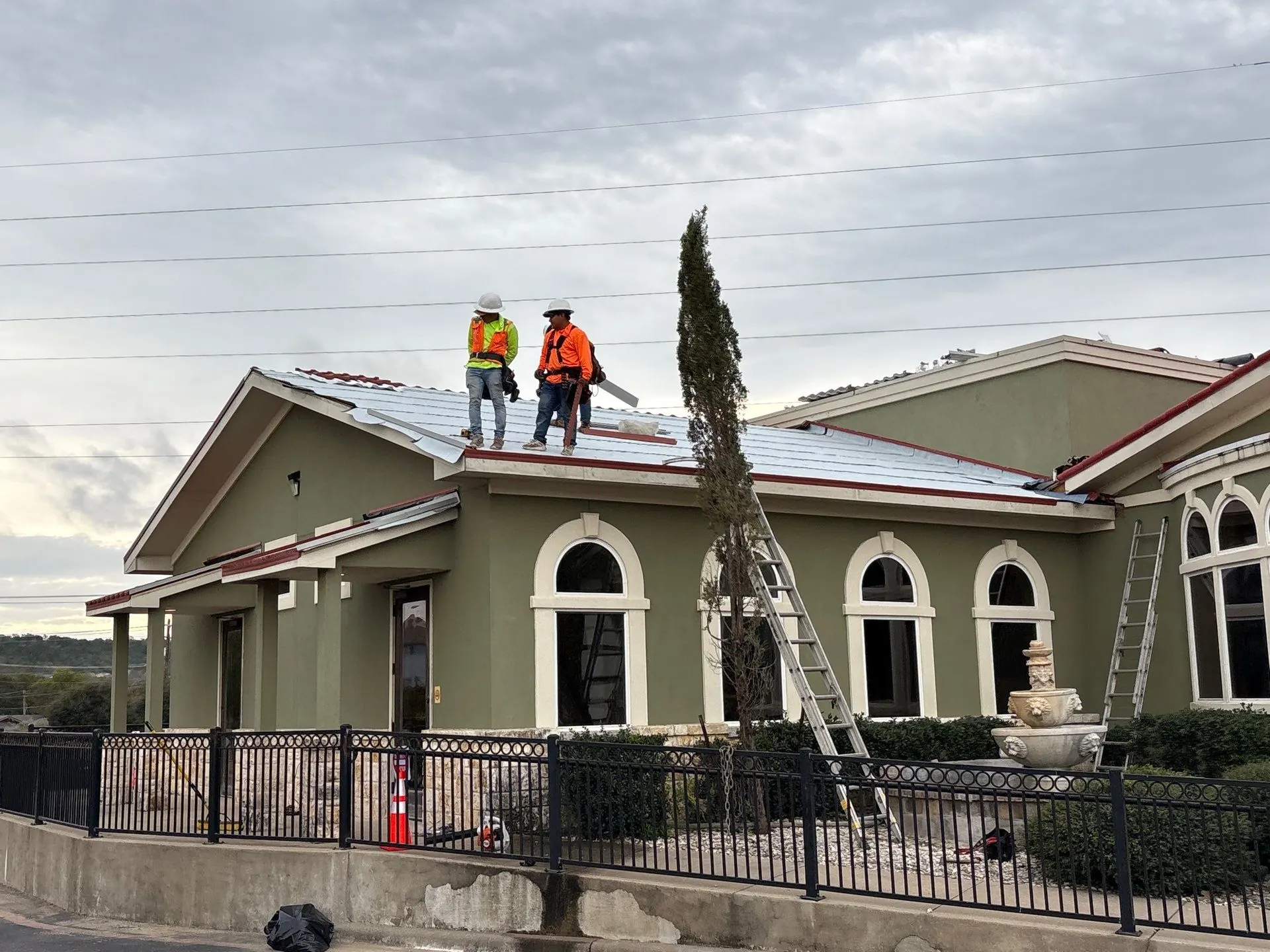 Roofers in harnesses and hard hats on new high-temperature underlayment above the arched windows of a restaurant during roof replacement