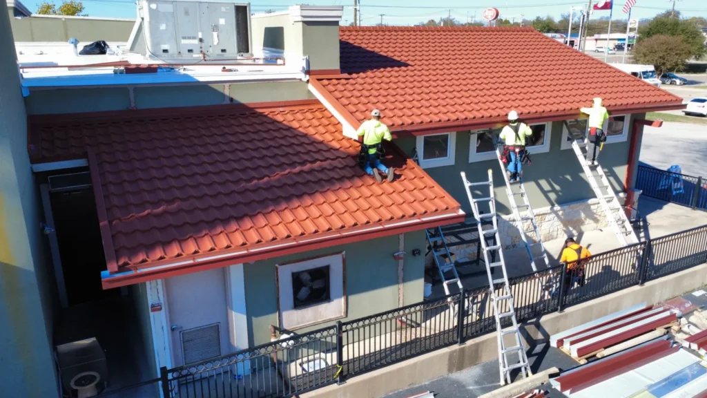 Crew installing red Worthouse metal tile roofing at Giovanni's Italian Restaurant in San Antonio, TX, with the white flat roof behind