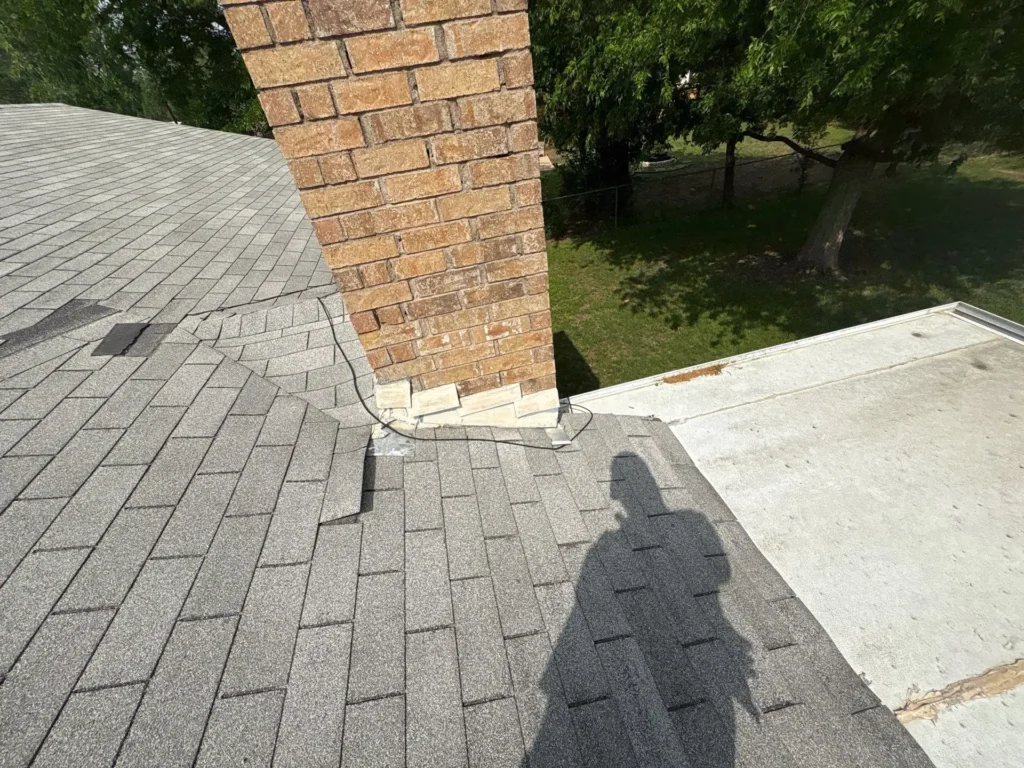 Loose chimney flashing, lifted shingles, and a failing seam on the low-slope roof of a Georgetown, TX home