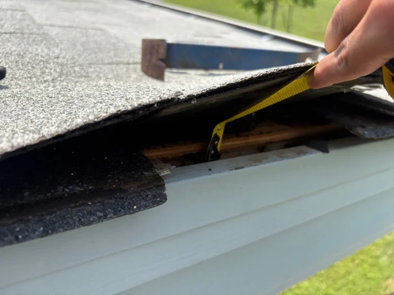 Tape measure under a lifted shingle at the roof edge showing damaged underlayment on a Georgetown, TX home
