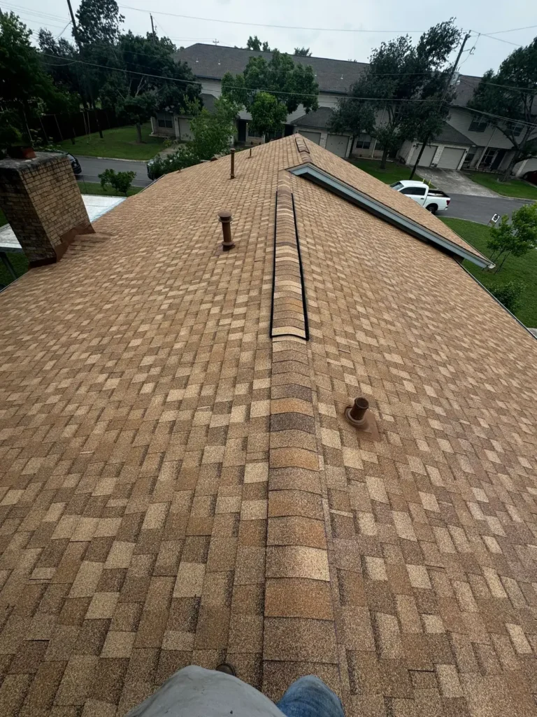 New tan architectural shingle roof with ridge vent, painted pipe vents, and chimney flashing on a Georgetown, TX home