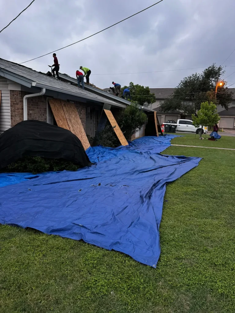 Roofing crew tearing off old shingles while tarps cover the lawn and plywood shields the windows of a Georgetown