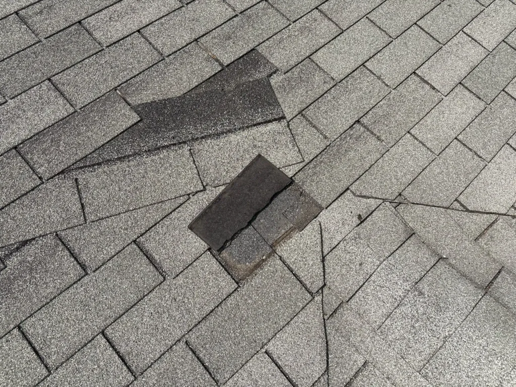 Torn and displaced shingle tabs next to a mismatched patch from an earlier repair on a Georgetown roof