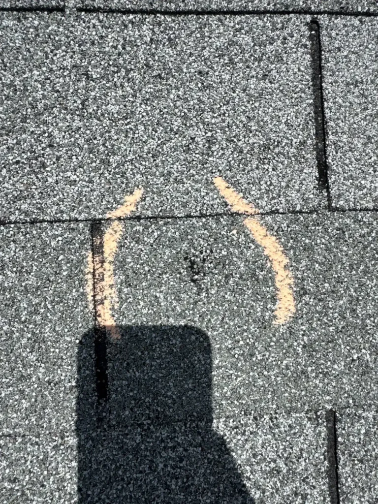 Close-up of a hail-damaged shingle with exposed mat marked for documentation