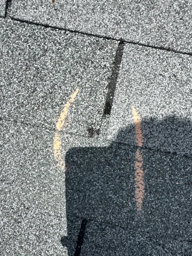 Hail impact on an asphalt shingle circled in chalk during inspection