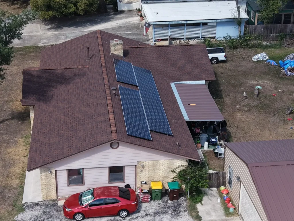 Aerial view of a new shingle roof with solar panels reinstalled and a new brown metal patio roof on a Helotes, TX