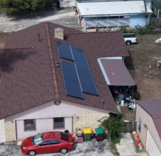 Aerial view of a new shingle roof with solar panels reinstalled and a new brown metal patio roof on a Helotes, TX