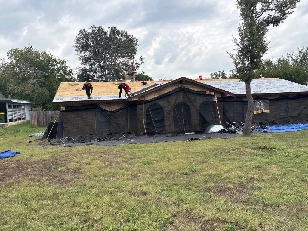 oofing crew installing ABC synthetic underlayment while Catch-All debris netting protects a brick home in Helotes,