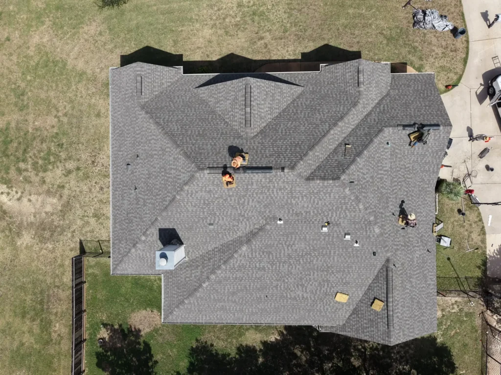 Aerial view of a new shingle roof on a Liberty Hill, TX home as the crew installs the final ridge vents