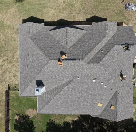 Aerial view of a new shingle roof on a Liberty Hill, TX home as the crew installs the final ridge vents