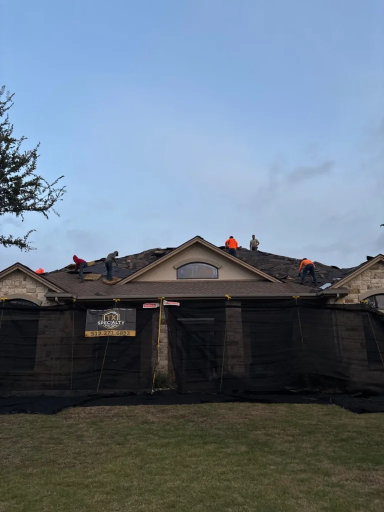 Roofing crew tearing off old shingles on a Liberty Hill home while Catch-All debris netting protects the front of the house