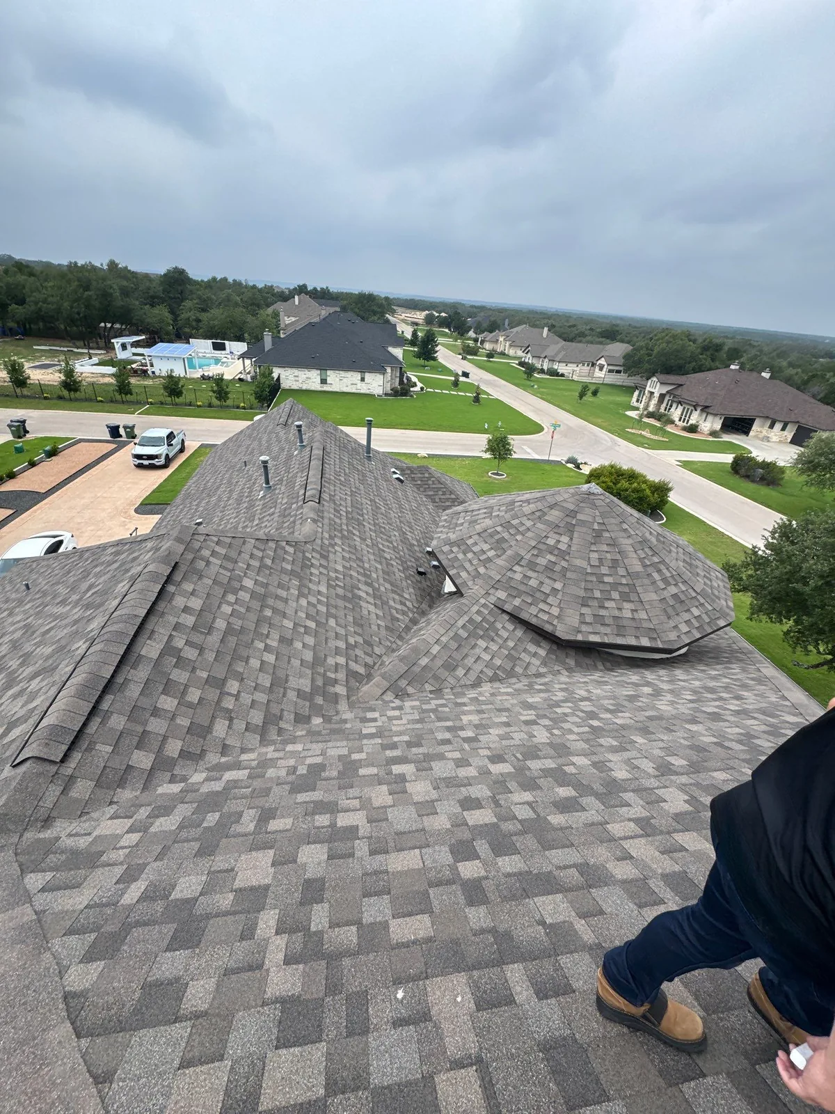 High-angle view of a large luxury home roof with architectural shingles, multiple hips, ridges and roof sections.