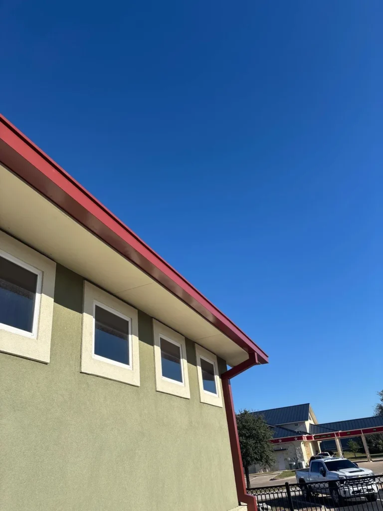 Red 6-inch commercial gutter running along the eave of a restaurant above square windows