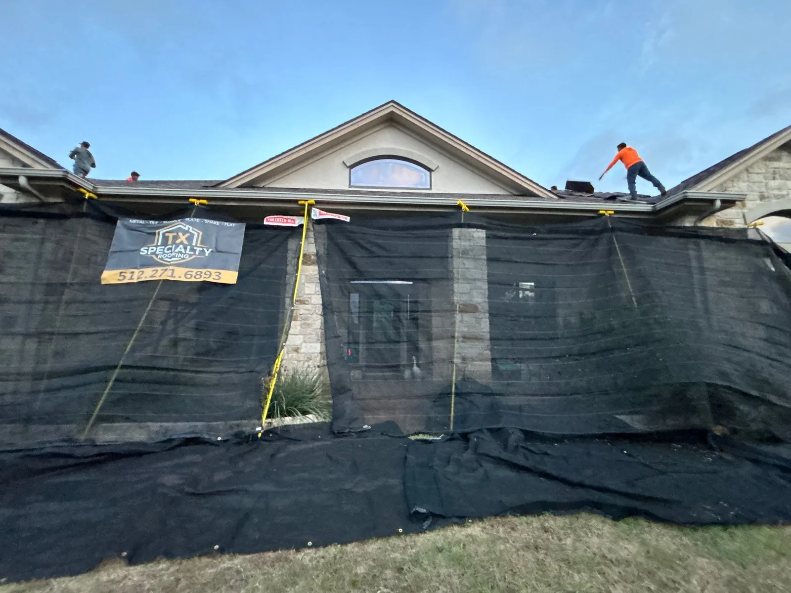 Protective Catch-All style netting installed across the front of a home while a roofing crew works on the roof.