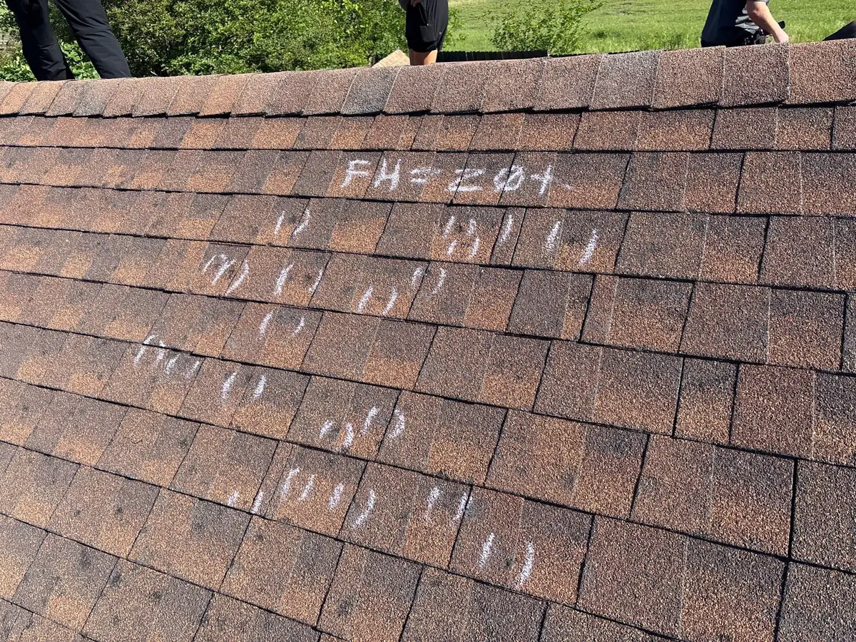 Asphalt shingle roof slope and ridge with multiple chalk marks identifying roof inspection findings.