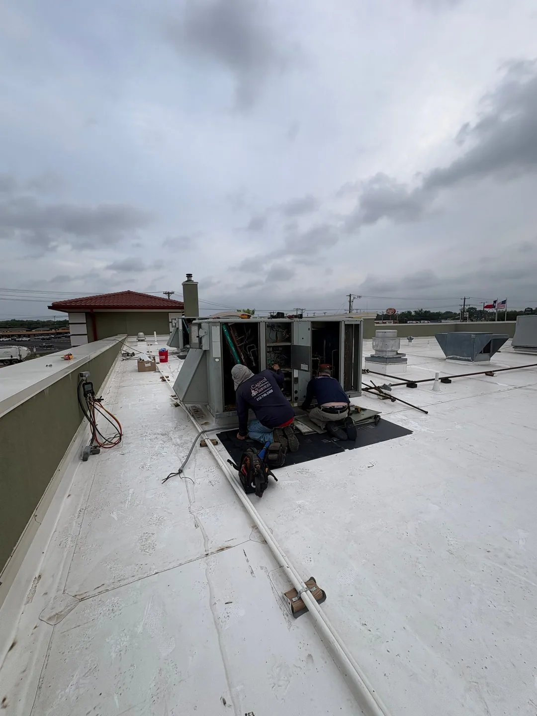 HVAC technicians servicing a rooftop unit on a new white PVC flat roof, working on protective pads
