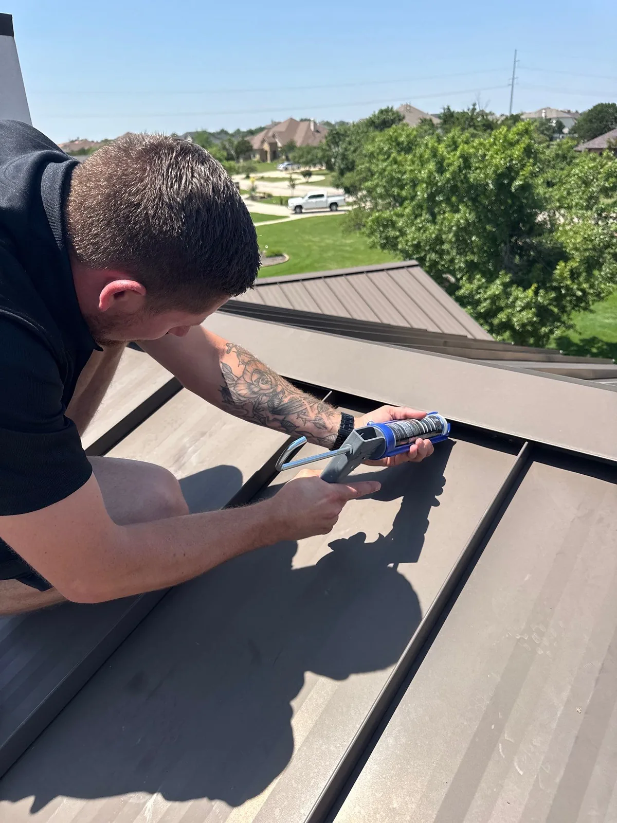 Roofing technician applying sealant along a standing seam metal roof detail during a maintenance repair.