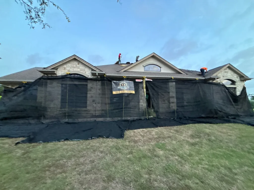 Texas Specialty Roofing crew working above a home protected by full-height debris netting during a roof replacement.