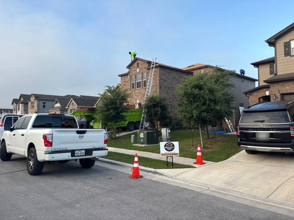 TX Specialty Roofing crew working on a roof replacement on a two-story brick home in Uhland, TX with the dump trailer staged