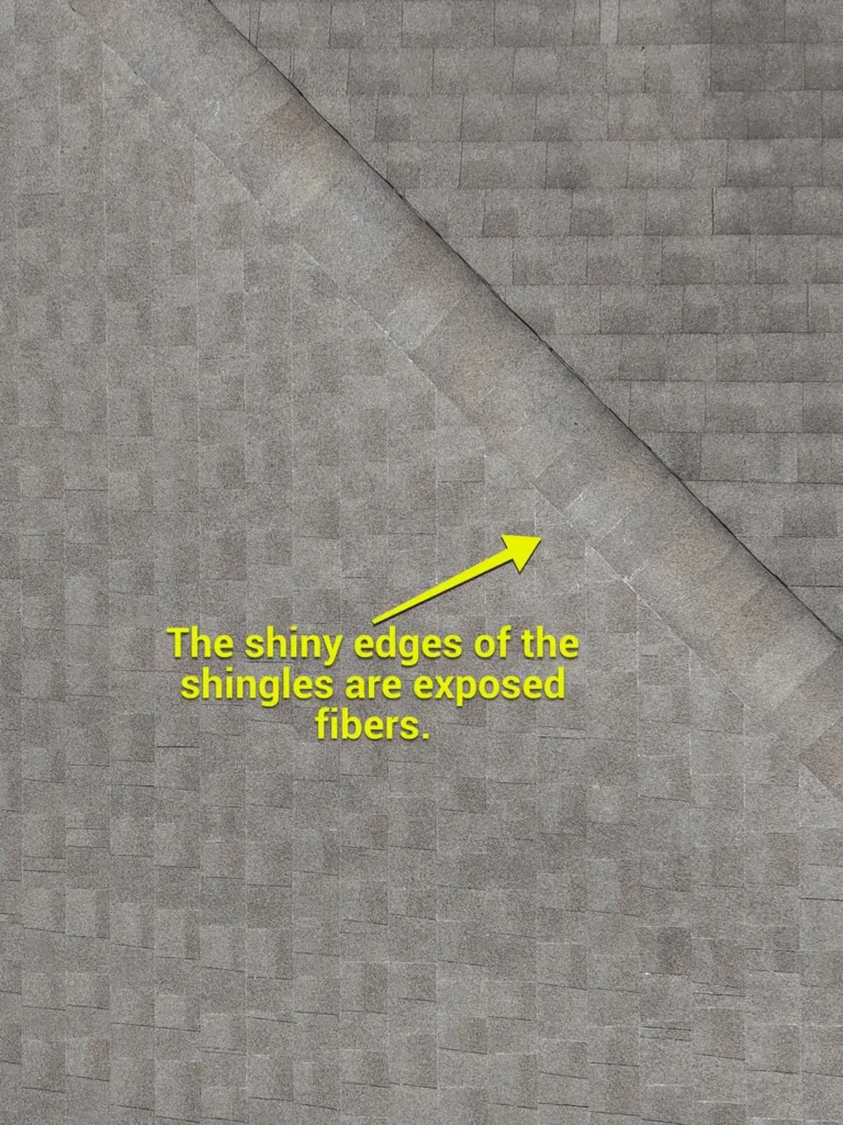 Close-up of worn asphalt shingles with shiny exposed fiberglass along the edges on a Liberty Hill roof