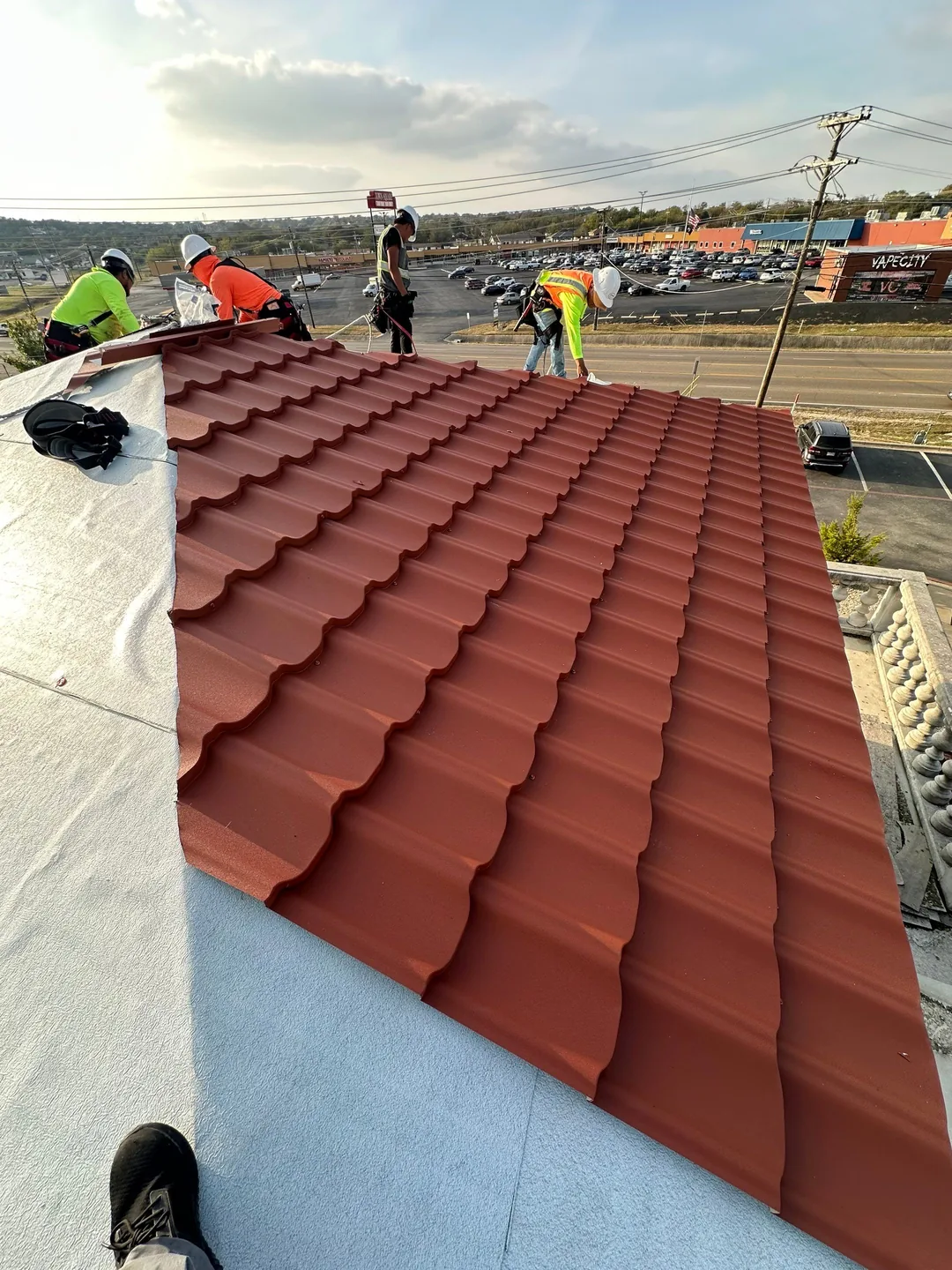 Close-up of red Worthouse Mediterranean metal tile panels being installed over white underlayment on a commercial restaurant roof